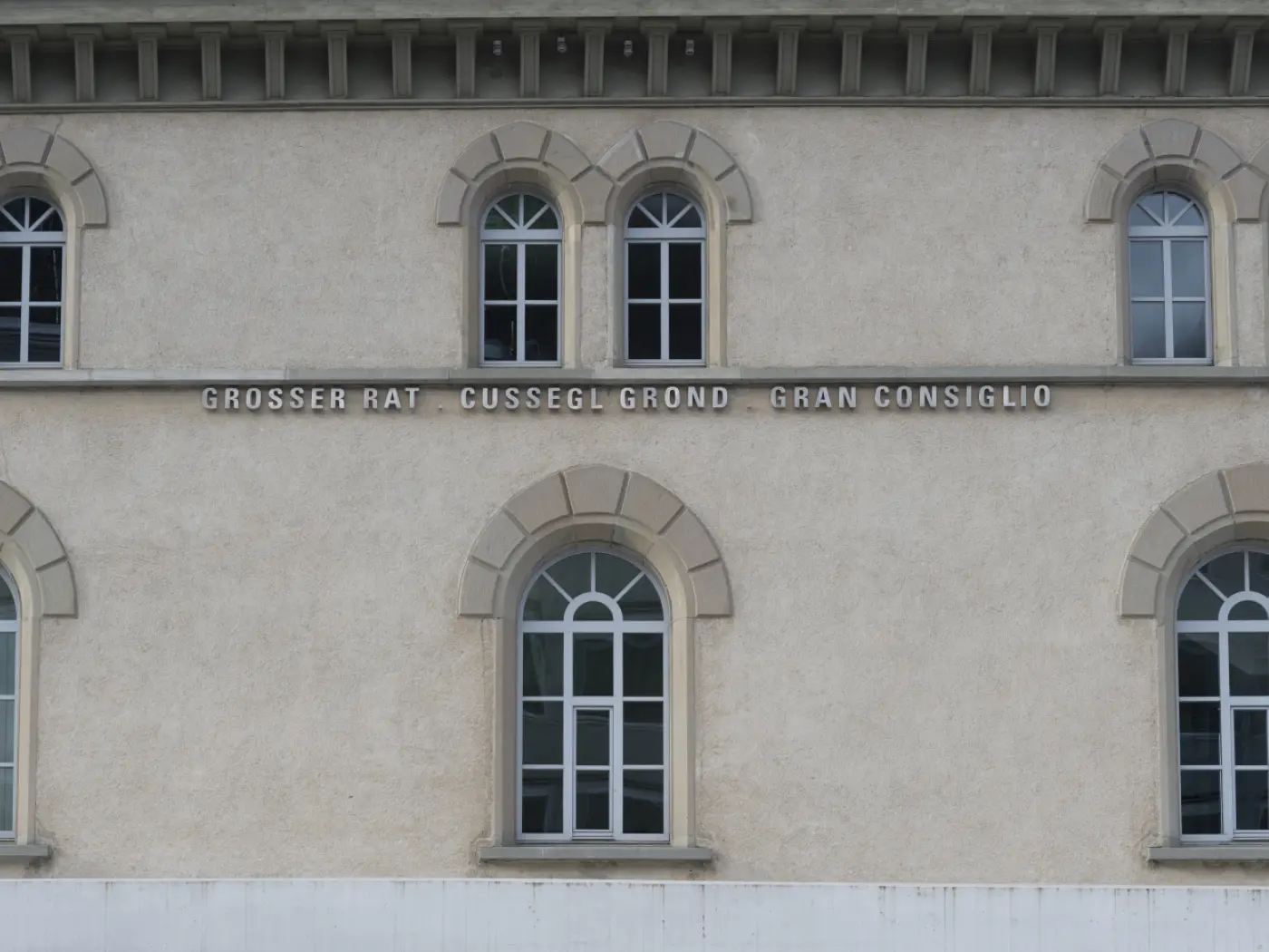 Façade di un edificio con finestre ad arco e iscrizioni in tre lingue: "GROSSER RAT", "CUSSEG GLOND", e "GRAN CONSIGLIO".