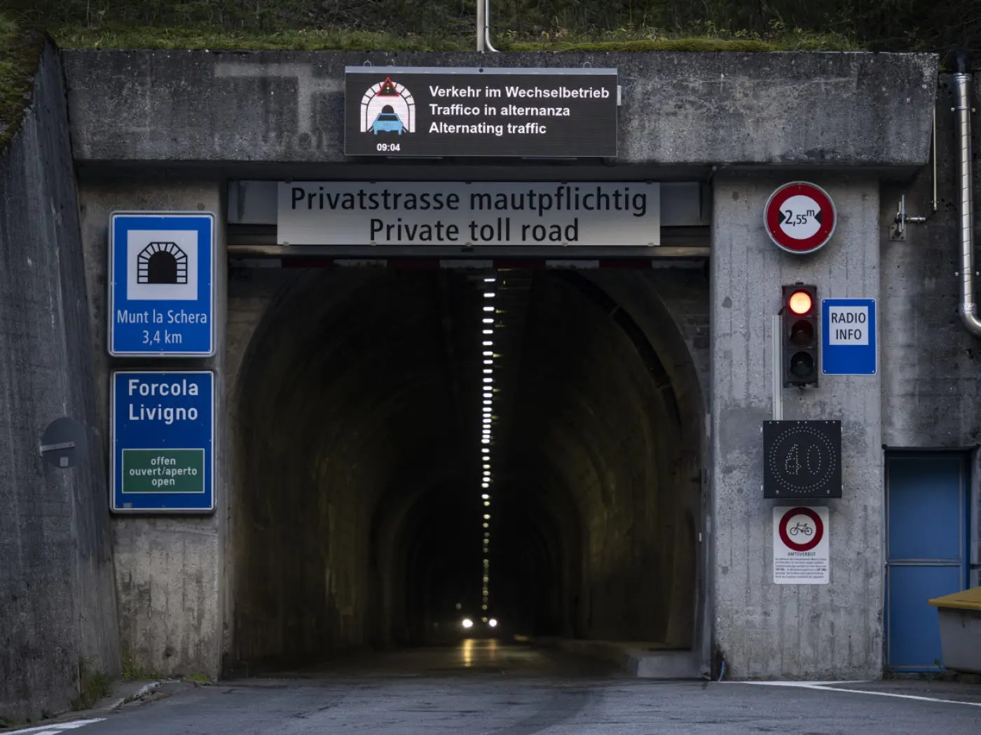 Ingresso di un tunnel con segnali stradali che indicano una strada privata a pedaggio, limite di velocità di 60 km/h e informazioni sul traffico alternato.