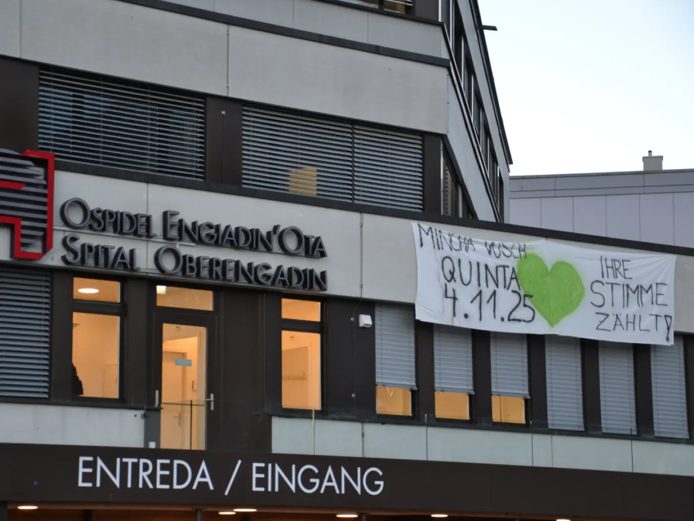 Insegna dell'ospedale Engiadin'Ota con un grande striscione che invita a votare il 4 novembre. Il messaggio è evidenziato con un cuore verde.