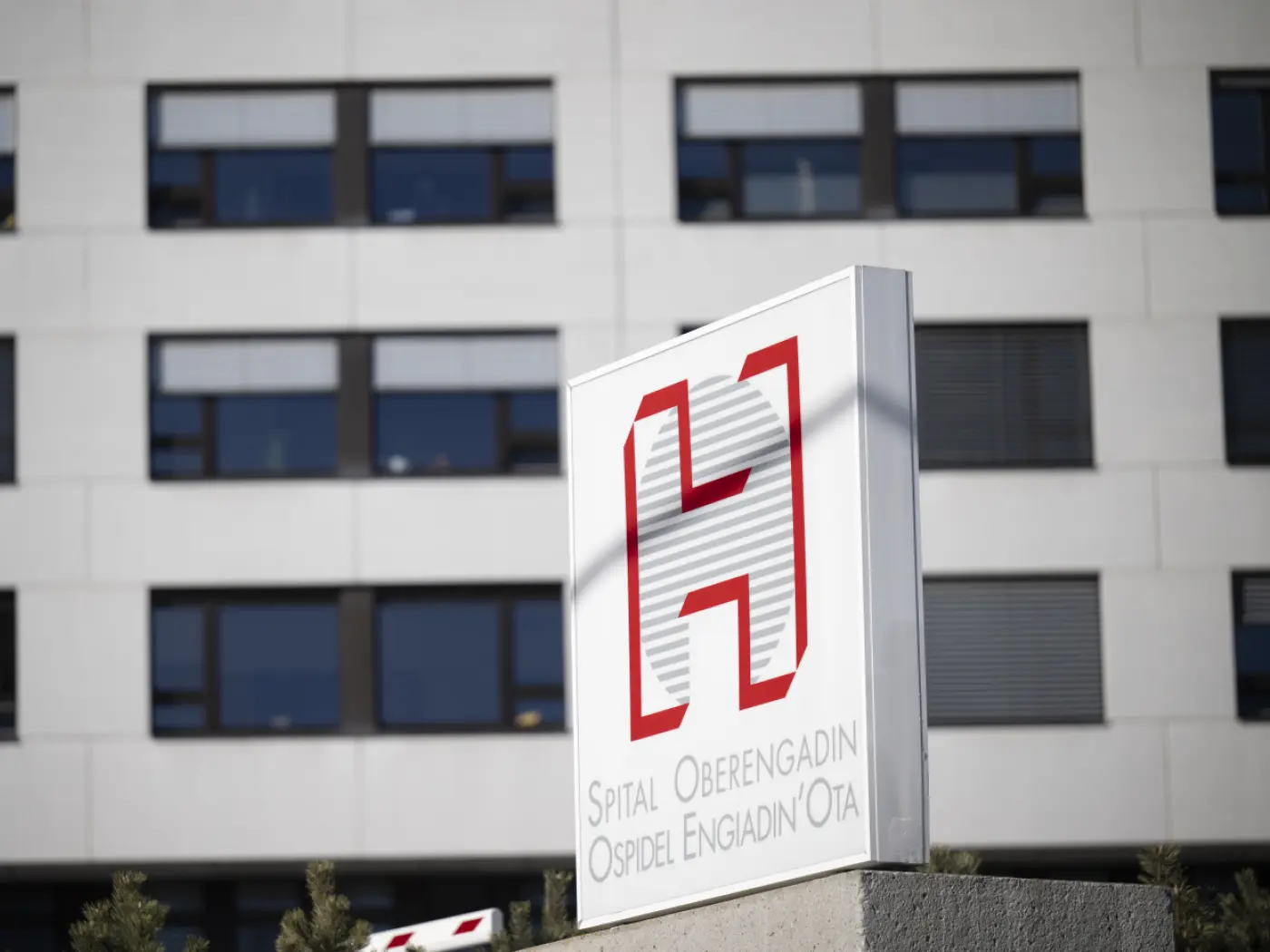 Insegna del Spital Oberengadin, Ospidal Engiadin'Ota, con il logo rosso su sfondo bianco in un contesto moderno. Finestroni dell'edificio in secondo piano.