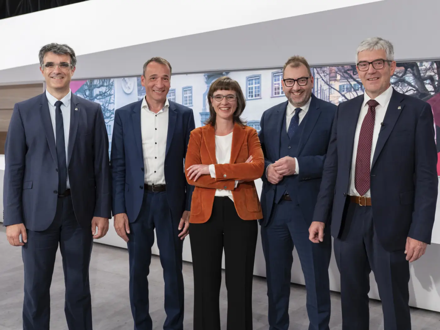 Gruppo di cinque persone in abbigliamento formale che sorridono, posando insieme in un ambiente moderno e luminoso.