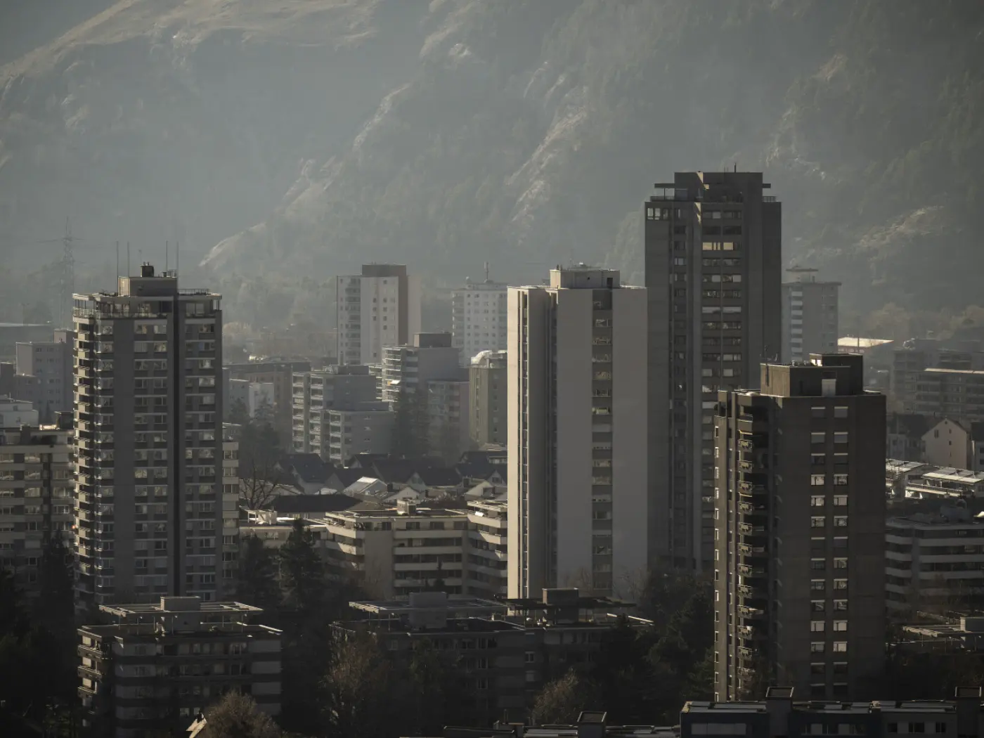 Veduta di un paesaggio urbano con grattacieli e edifici residenziali. Sullo sfondo si intravede una catena montuosa in lontananza,