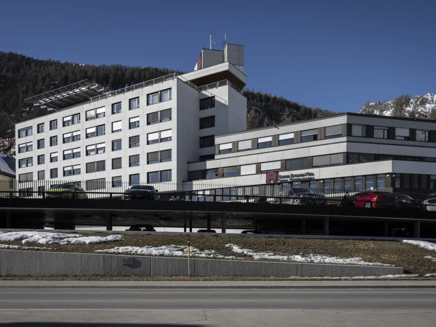 Edificio moderno a più piani con una facciata bianca e finestre scure, situato in un'area montuosa. Sullo sfondo, si vedono le montagne